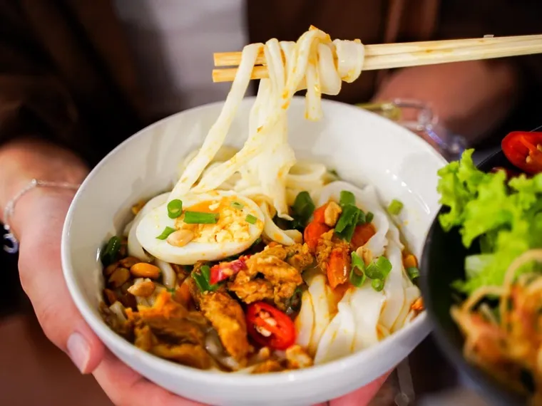 Mi Quang features thick, chewy rice noodles—handcrafted from soaked rice and steamed into sheets—perfectly pairing with rich, flavorful toppings. Image Source: helio.vn