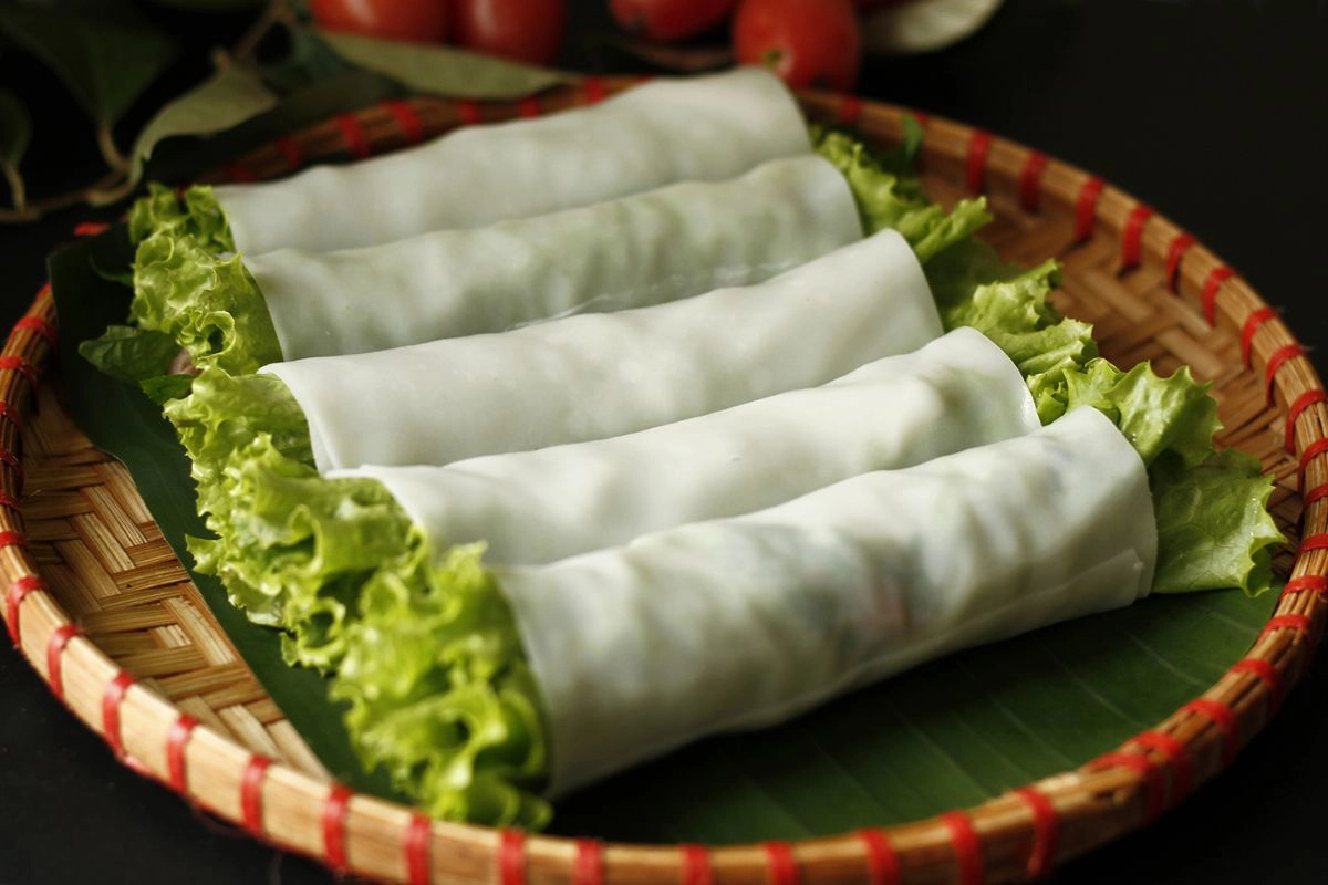 Freshly rolled Pho Cuon stacked neatly on a plate next to a small bowl of savory fish sauce