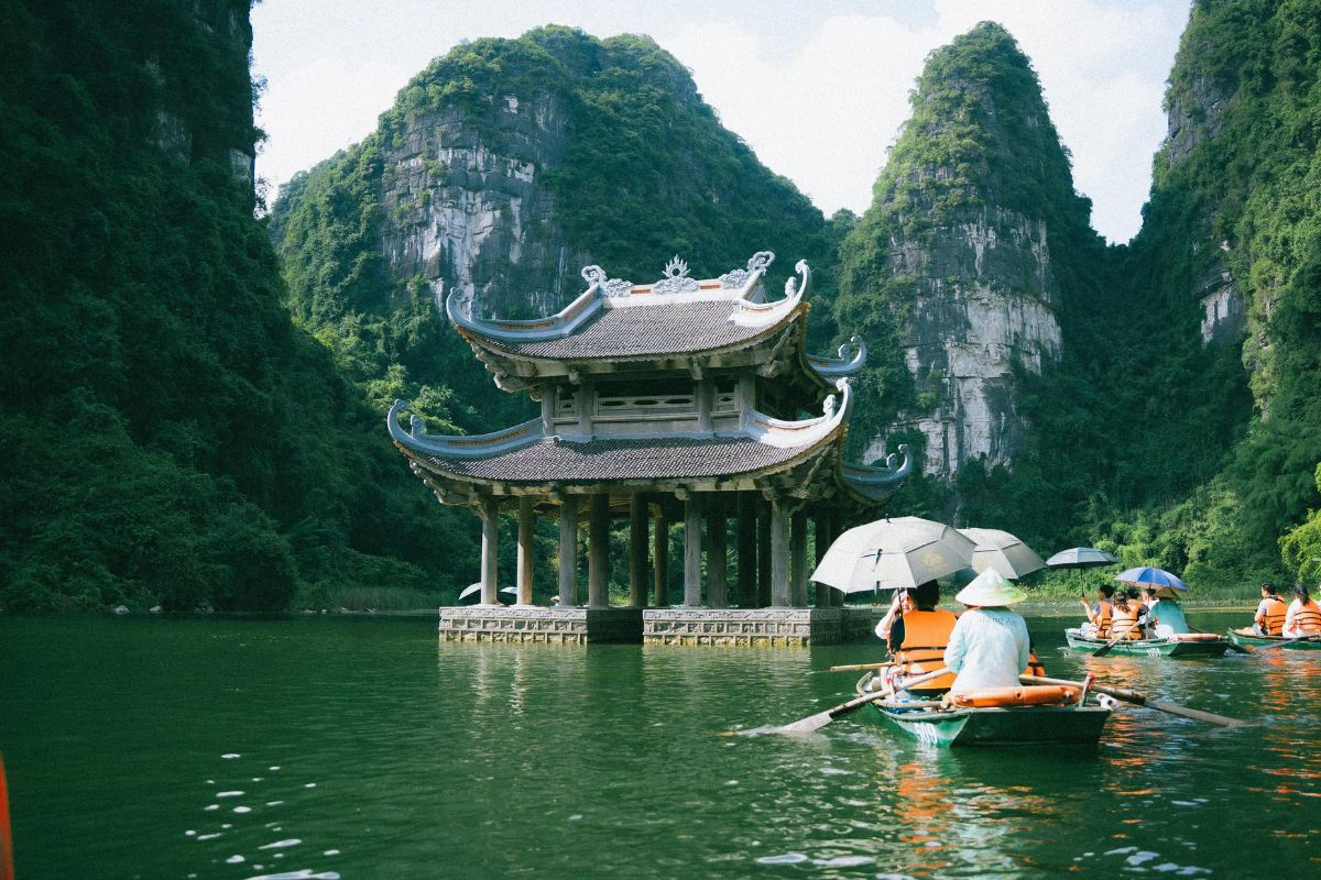 Tam Coc boats pass rice fields beneath dramatic limestone cliffs 