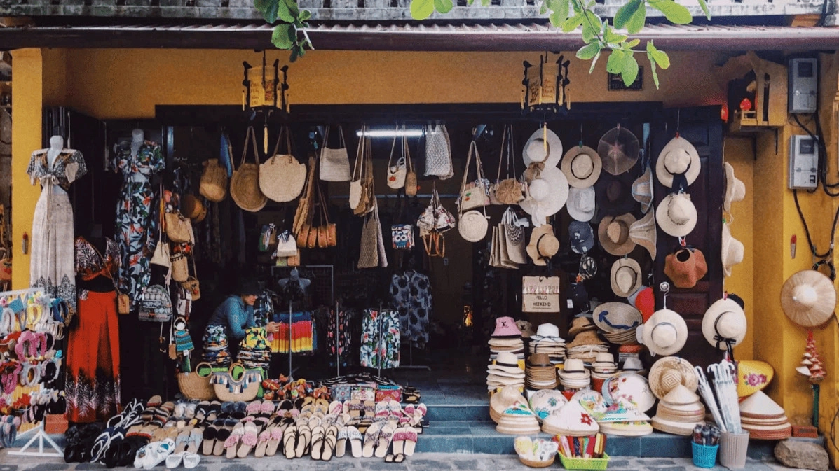 Colorful shop overflowing with woven hats, bags, and sandals lines a charming yellow storefront 