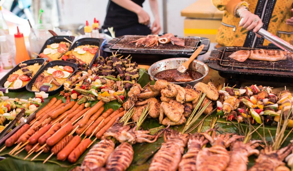 Grilled skewers, sausages, and squid sizzle side by side at a bustling night market food stall 